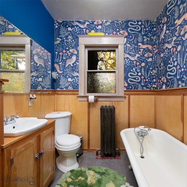 bathroom featuring radiator, vanity, wooden walls, a tub to relax in, and toilet