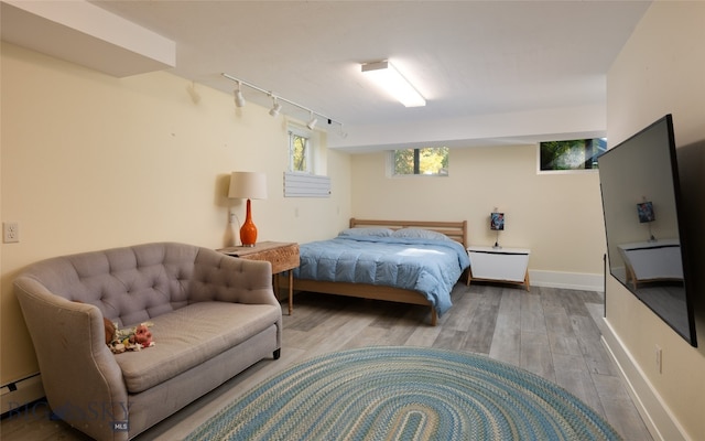 bedroom featuring rail lighting, baseboard heating, and light hardwood / wood-style flooring