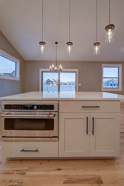 kitchen featuring white cabinetry, hanging light fixtures, stainless steel oven, and light wood-type flooring