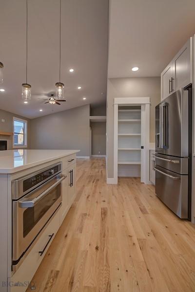 kitchen featuring appliances with stainless steel finishes, light hardwood / wood-style floors, hanging light fixtures, and white cabinets