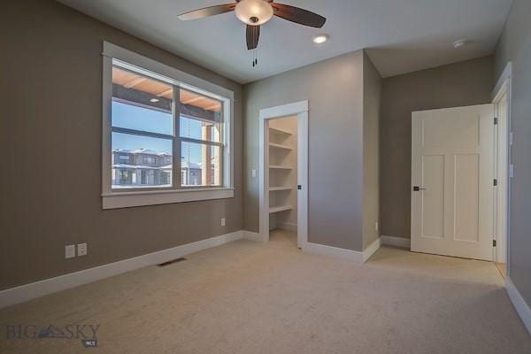 unfurnished bedroom featuring a spacious closet, light colored carpet, and ceiling fan