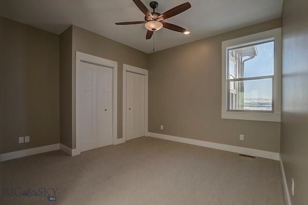 unfurnished bedroom with ceiling fan, multiple closets, and carpet