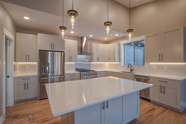 kitchen featuring a kitchen island, appliances with stainless steel finishes, pendant lighting, sink, and wall chimney range hood