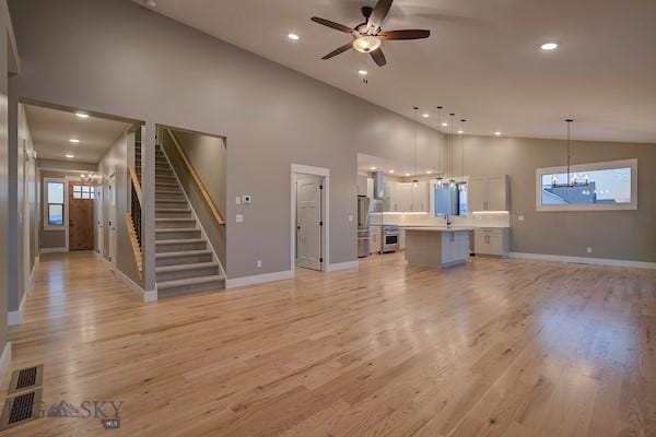 unfurnished living room featuring ceiling fan with notable chandelier, high vaulted ceiling, and light wood-type flooring