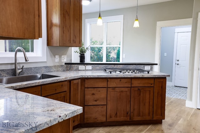 kitchen featuring stainless steel gas stovetop, light hardwood / wood-style flooring, decorative light fixtures, and sink