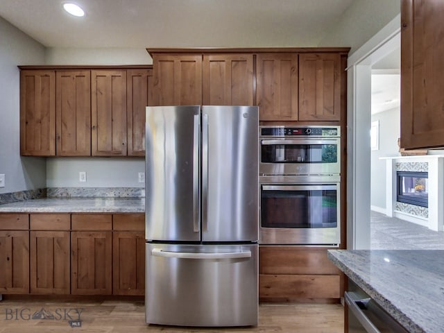 kitchen featuring a multi sided fireplace, light stone countertops, stainless steel appliances, and light hardwood / wood-style floors