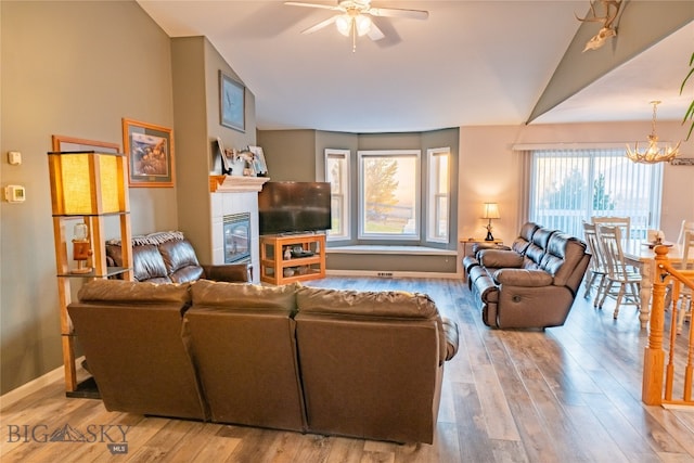 living room with a healthy amount of sunlight, lofted ceiling, light hardwood / wood-style flooring, and ceiling fan with notable chandelier