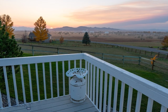 deck at dusk with a rural view, a yard, and a mountain view