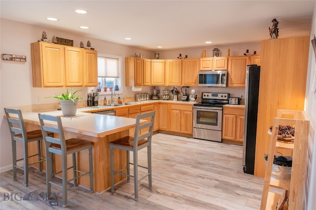 kitchen featuring a breakfast bar area, light hardwood / wood-style flooring, kitchen peninsula, stainless steel appliances, and sink