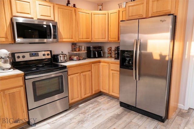 kitchen with light brown cabinetry, stainless steel appliances, and light hardwood / wood-style floors