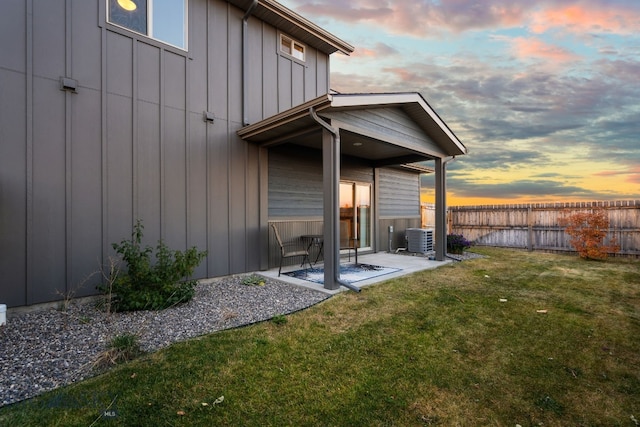 back house at dusk featuring a patio, central AC unit, and a lawn