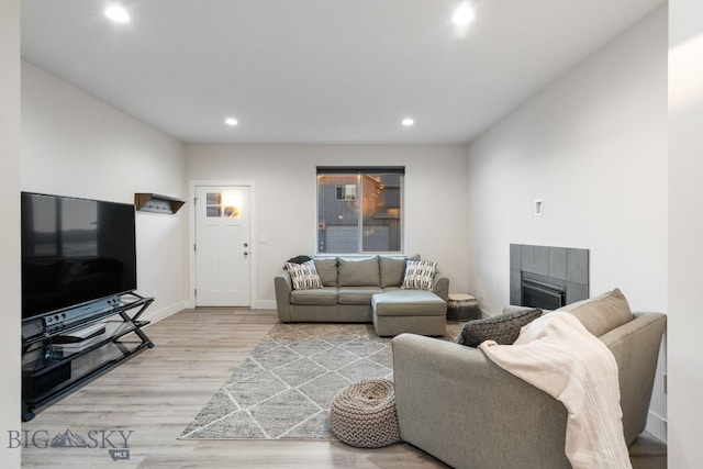 living room with a tiled fireplace and light wood-type flooring