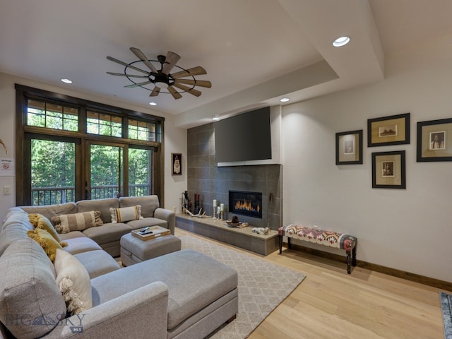 living room featuring light hardwood / wood-style flooring, a tile fireplace, and ceiling fan