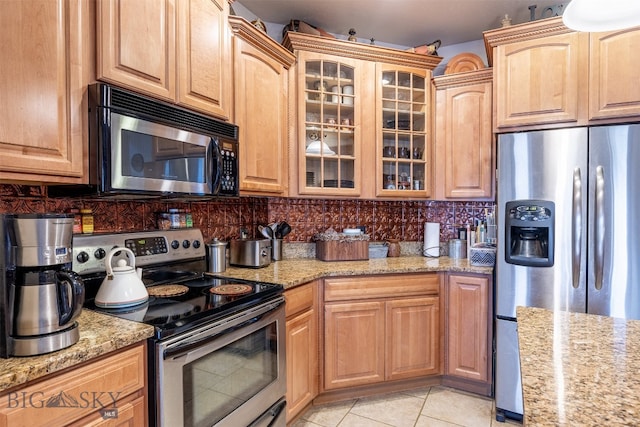 kitchen with appliances with stainless steel finishes, light stone countertops, backsplash, and light tile patterned floors