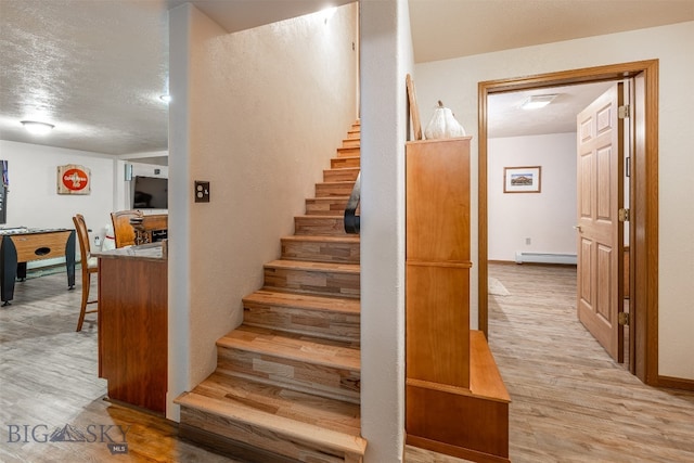 stairs featuring hardwood / wood-style flooring, a textured ceiling, and a baseboard heating unit