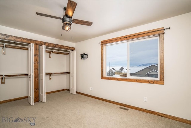 unfurnished bedroom with multiple closets, ceiling fan, and light carpet