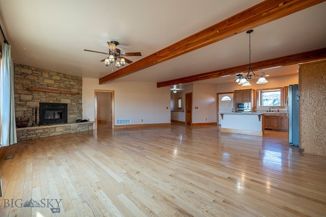 unfurnished living room with beam ceiling, light wood-type flooring, ceiling fan with notable chandelier, a stone fireplace, and sink