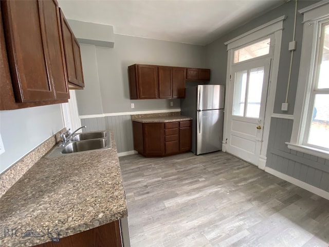 kitchen featuring light wood-type flooring, sink, light stone counters, and stainless steel refrigerator