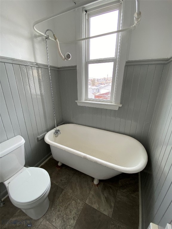 bathroom with a washtub, wood walls, and toilet