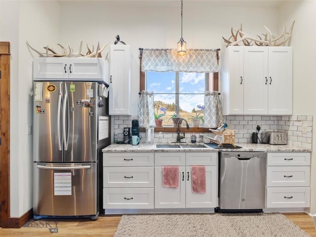 kitchen with a sink, stainless steel appliances, white cabinets, backsplash, and light stone counters