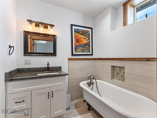 full bath featuring tile walls, a freestanding bath, wood finished floors, and vanity