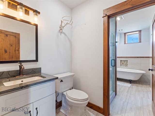 full bathroom featuring toilet, vanity, a shower stall, a freestanding bath, and baseboards