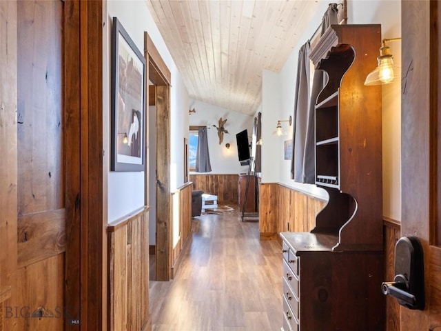 hallway with lofted ceiling, wooden ceiling, wainscoting, wooden walls, and wood finished floors