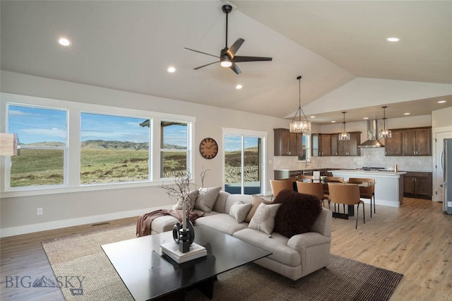 living room with vaulted ceiling, ceiling fan, and light wood-type flooring