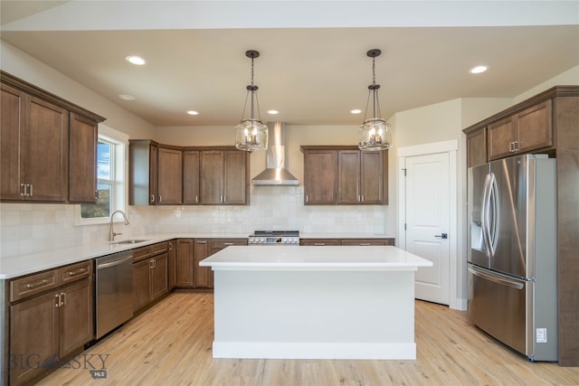 kitchen with sink, hanging light fixtures, stainless steel appliances, a center island, and wall chimney exhaust hood