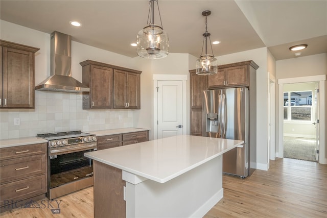 kitchen with a center island, wall chimney range hood, pendant lighting, stainless steel appliances, and backsplash