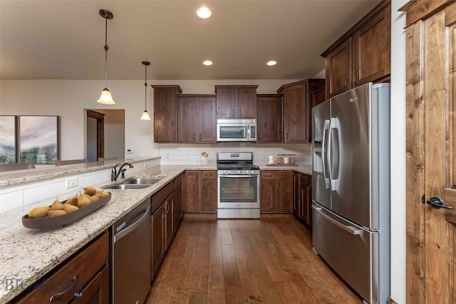 kitchen featuring dark hardwood / wood-style floors, stainless steel appliances, hanging light fixtures, and light stone counters