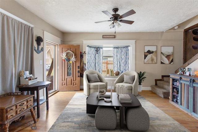 living area featuring ceiling fan, light wood-type flooring, and a textured ceiling