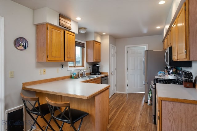 kitchen featuring a kitchen breakfast bar, kitchen peninsula, stainless steel appliances, sink, and light wood-type flooring