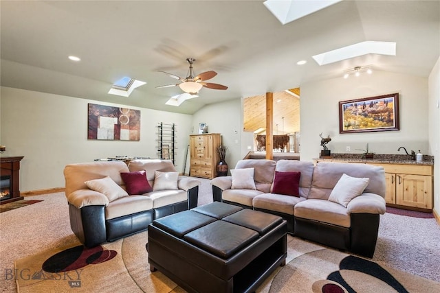 carpeted living room with ceiling fan and vaulted ceiling with skylight