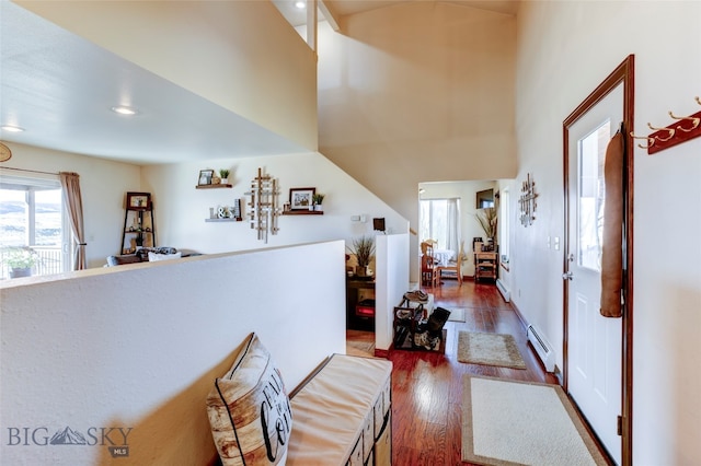 hallway featuring baseboard heating, a high ceiling, and dark hardwood / wood-style flooring