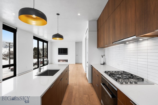 kitchen featuring sink, oven, light hardwood / wood-style flooring, stainless steel gas stovetop, and pendant lighting