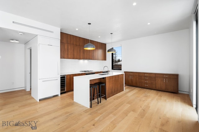 kitchen featuring a kitchen breakfast bar, light hardwood / wood-style floors, beverage cooler, hanging light fixtures, and a center island with sink