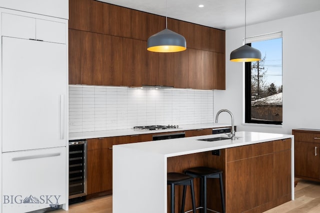 kitchen with pendant lighting, light hardwood / wood-style floors, decorative backsplash, wine cooler, and sink