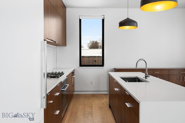 kitchen with hanging light fixtures, light hardwood / wood-style floors, tasteful backsplash, appliances with stainless steel finishes, and sink