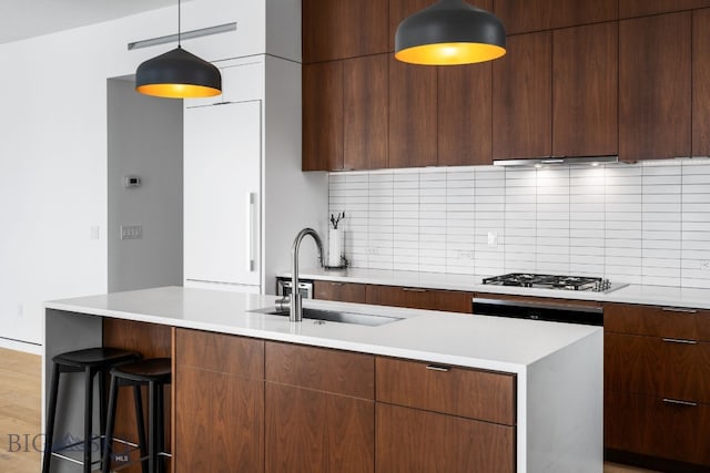 kitchen featuring decorative light fixtures, gas cooktop, decorative backsplash, a kitchen breakfast bar, and sink