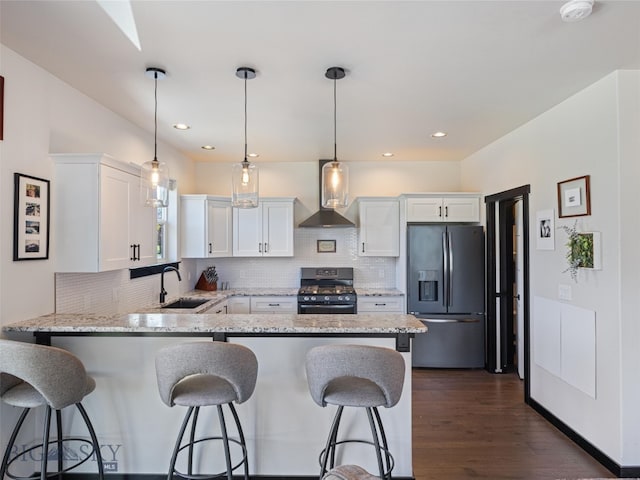 kitchen featuring wall chimney range hood, black range with gas stovetop, stainless steel refrigerator with ice dispenser, sink, and white cabinetry