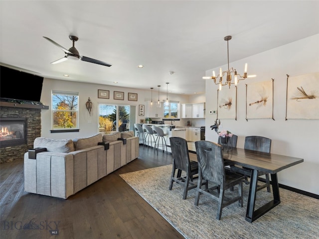 dining space featuring ceiling fan with notable chandelier, dark wood-type flooring, and a fireplace