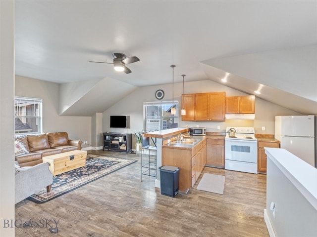 kitchen featuring lofted ceiling, hanging light fixtures, a kitchen breakfast bar, light wood-type flooring, and white appliances