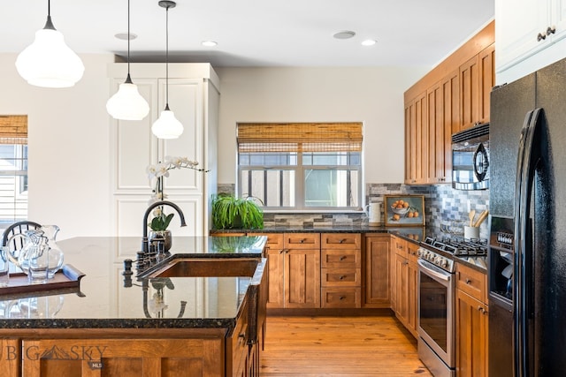 kitchen featuring a wealth of natural light, black appliances, light hardwood / wood-style floors, and dark stone counters