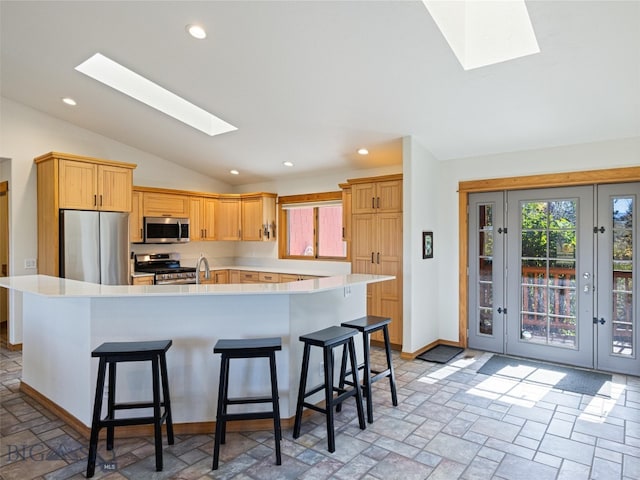 kitchen with a kitchen island with sink, stainless steel appliances, sink, vaulted ceiling with skylight, and a kitchen bar