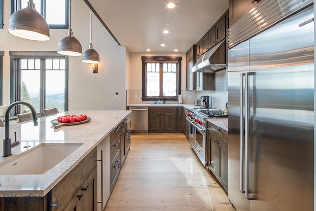 kitchen with light stone countertops, high end appliances, sink, pendant lighting, and light hardwood / wood-style floors