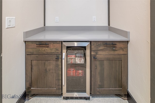 bar featuring dark brown cabinets, light tile patterned floors, and beverage cooler