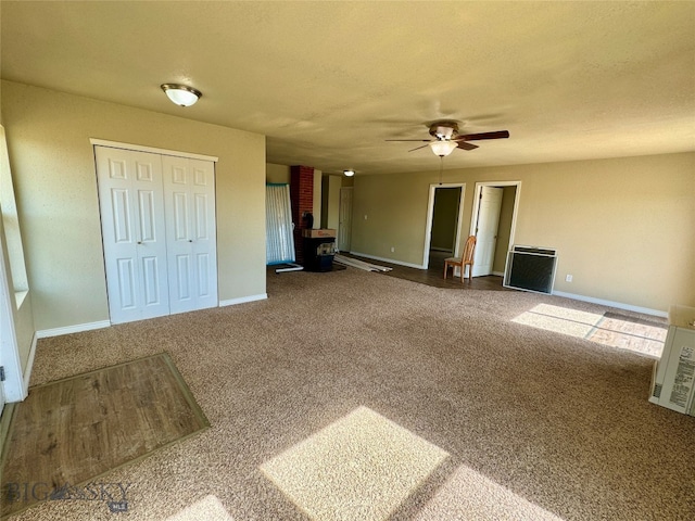 unfurnished living room with ceiling fan, a wood stove, and carpet floors