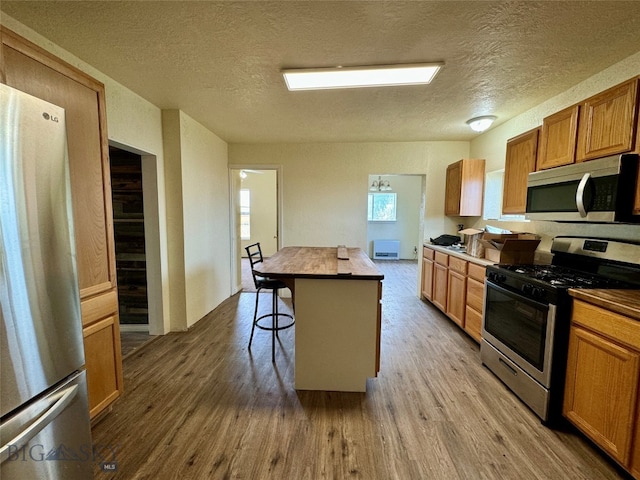 kitchen with stainless steel appliances, hardwood / wood-style floors, a textured ceiling, a breakfast bar area, and a kitchen island