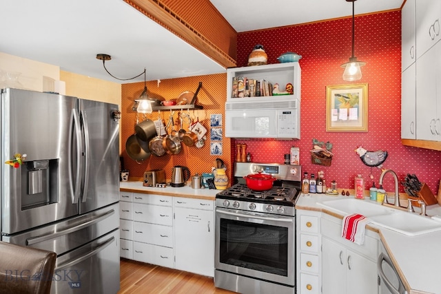 kitchen with stainless steel appliances, hanging light fixtures, sink, white cabinetry, and light wood-type flooring